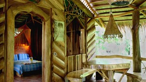 A wooden hut-style room with a bed, a table, and a hanging light fixture. - La Costa de Papito (Cahuita)