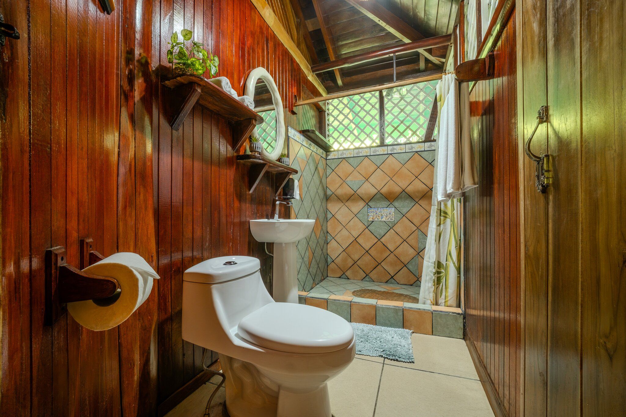 A wooden bathroom with a toilet, sink, and shower area.
