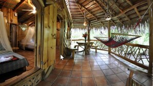 A rustic wooden room with a hammock, a bed, and a dining area. - La Costa de Papito (Cahuita)