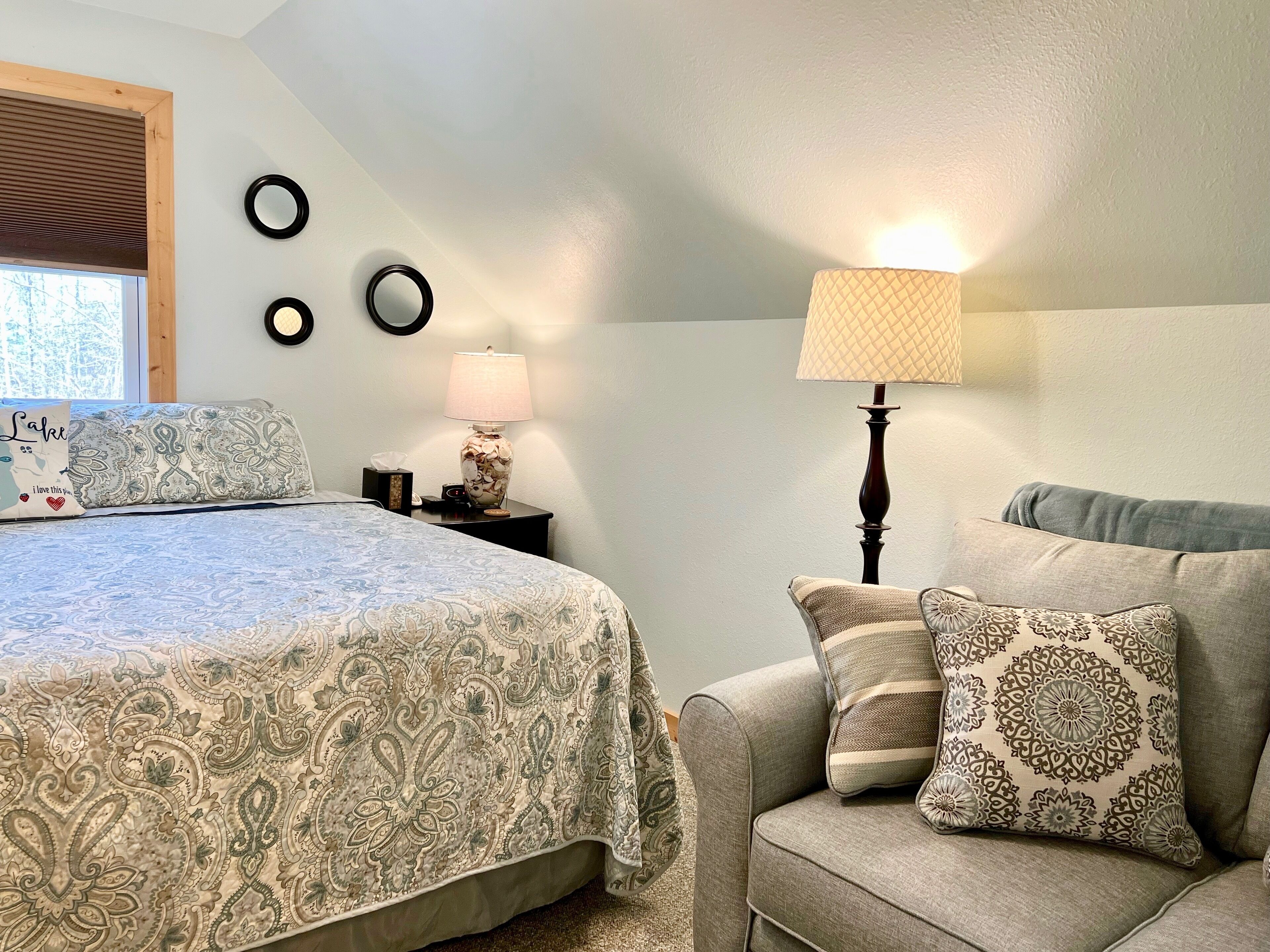 Un dormitorio con cama, mesita de noche, lámpara, sofá y elementos decorativos en la pared.