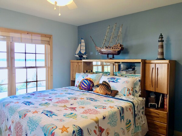 A bedroom with a bed covered in a colorful fish and coral print, wooden headboards, and a ship model on the wall. - Torch Lake Bed & Breakfast (Central Lake)