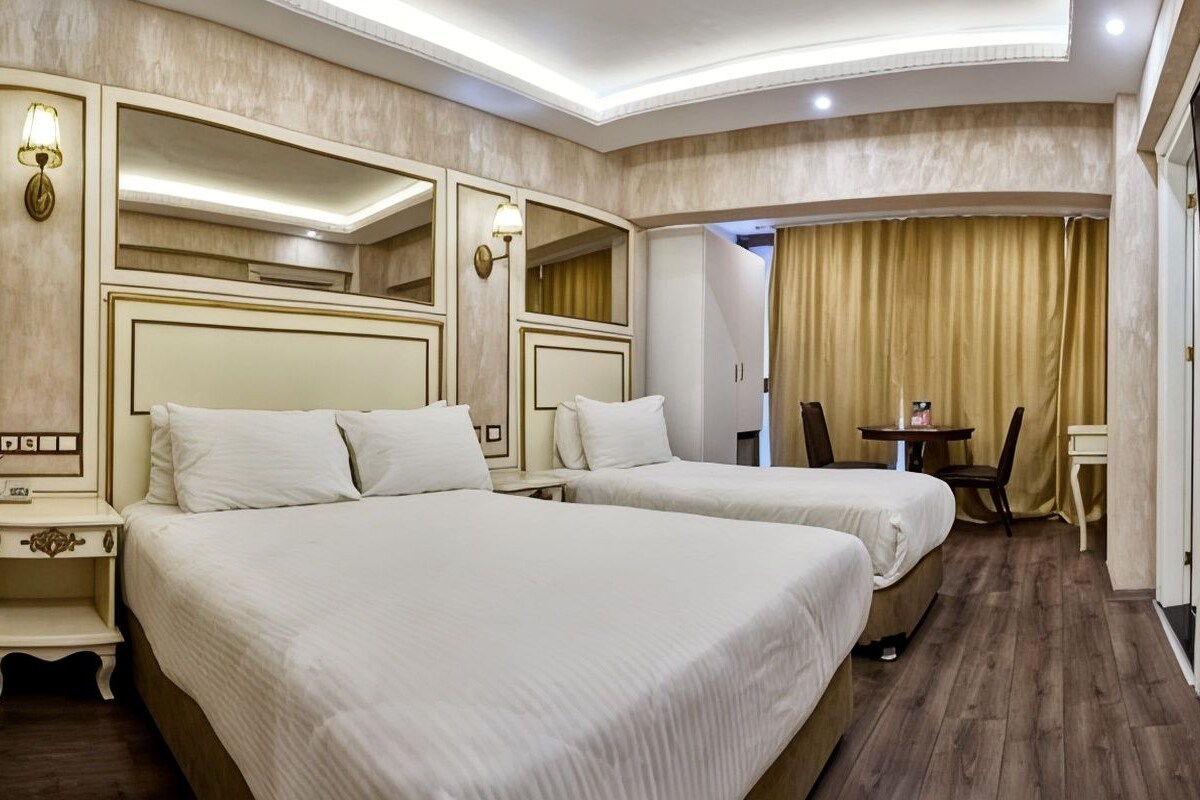 A hotel room with two beds, a desk, a chair, and a television.