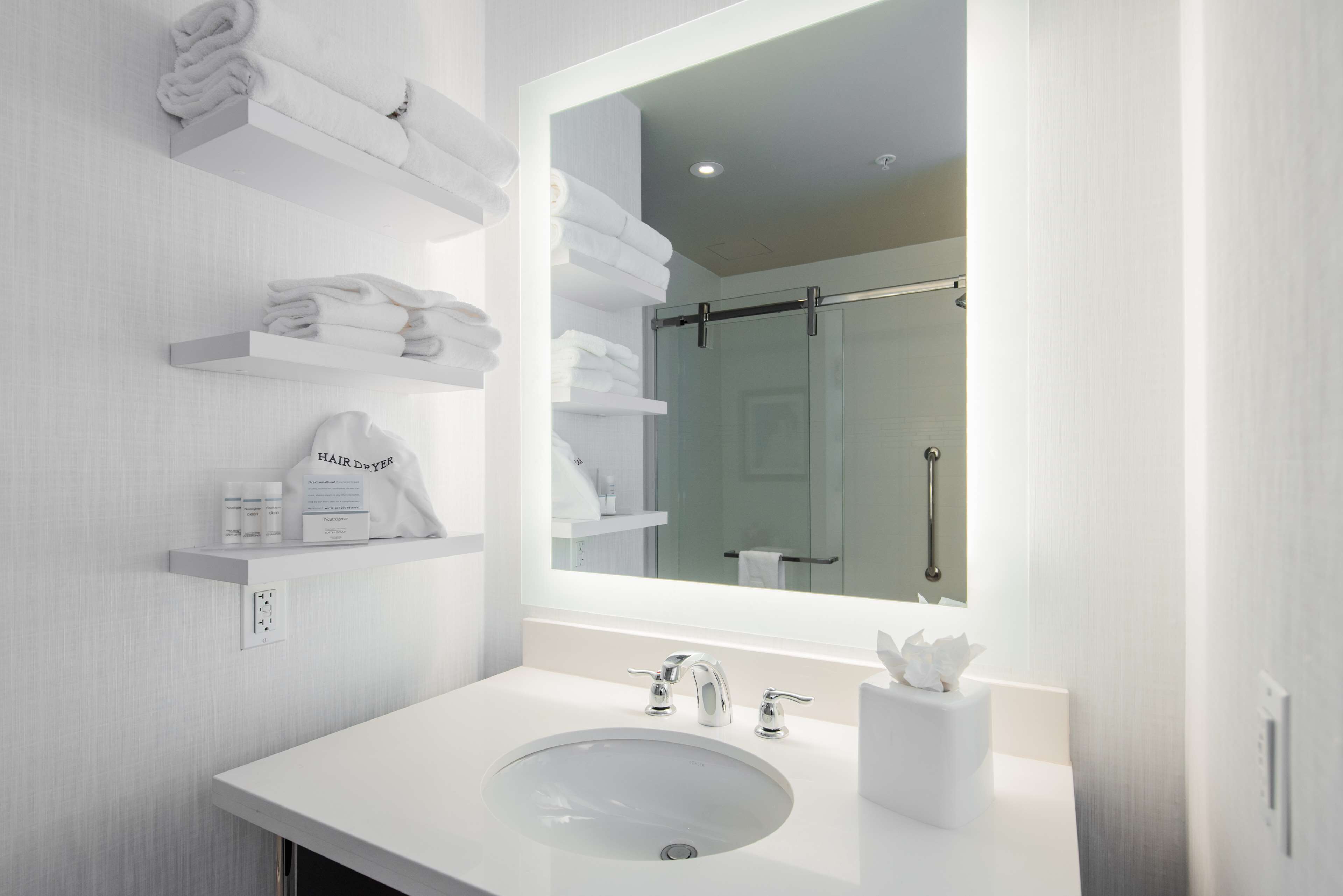 A modern bathroom with a large mirror, white sink, and towel storage on shelves.