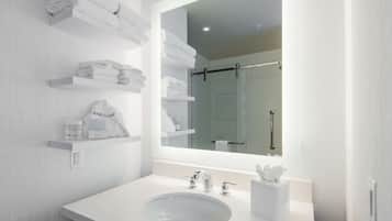 A modern bathroom with a large mirror, white sink, and towel storage on shelves.