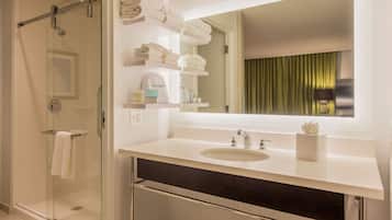 A modern bathroom with a glass shower enclosure, a large mirror, and neatly folded towels on shelves.