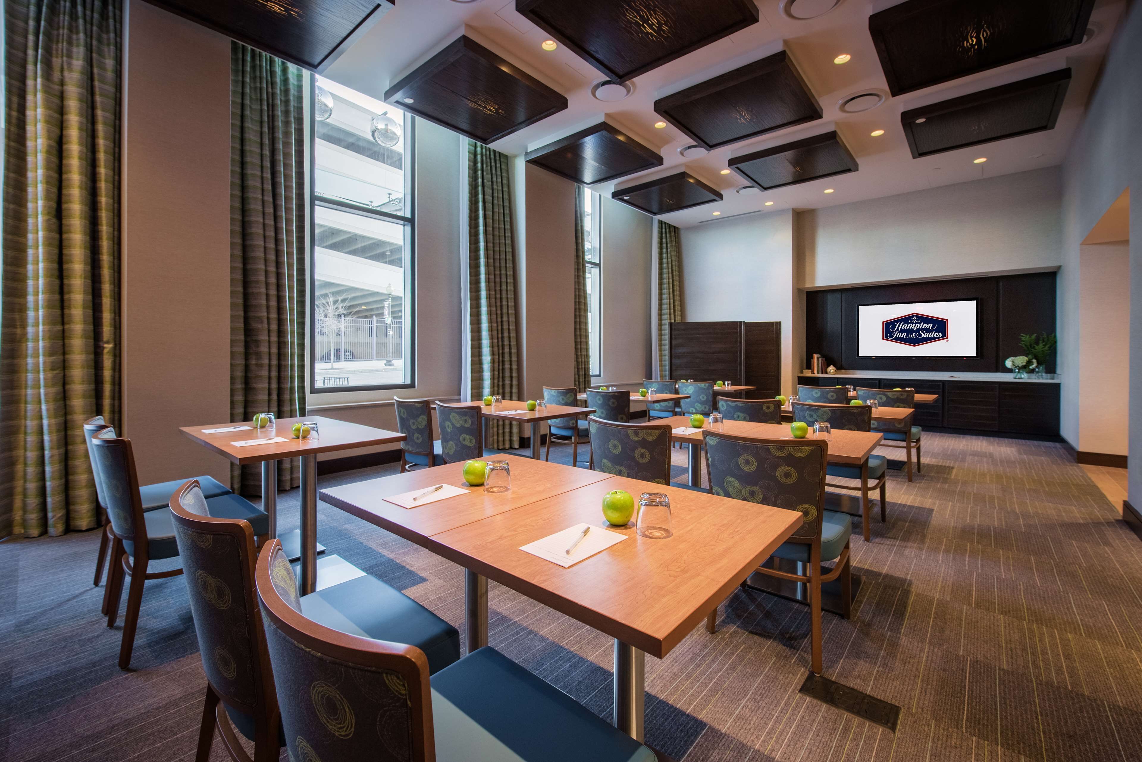 A hotel conference room with tables, chairs, a large screen, and a view of the city.