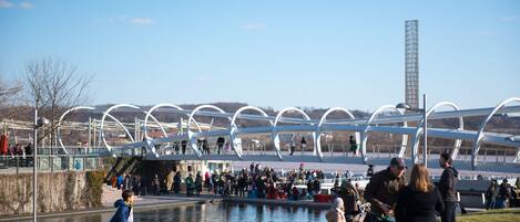 Un parque público con un puente moderno, un estanque y una torre alta.