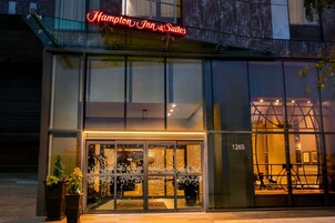 A modern hotel entrance with glass doors, a neon sign, and a visible room number.