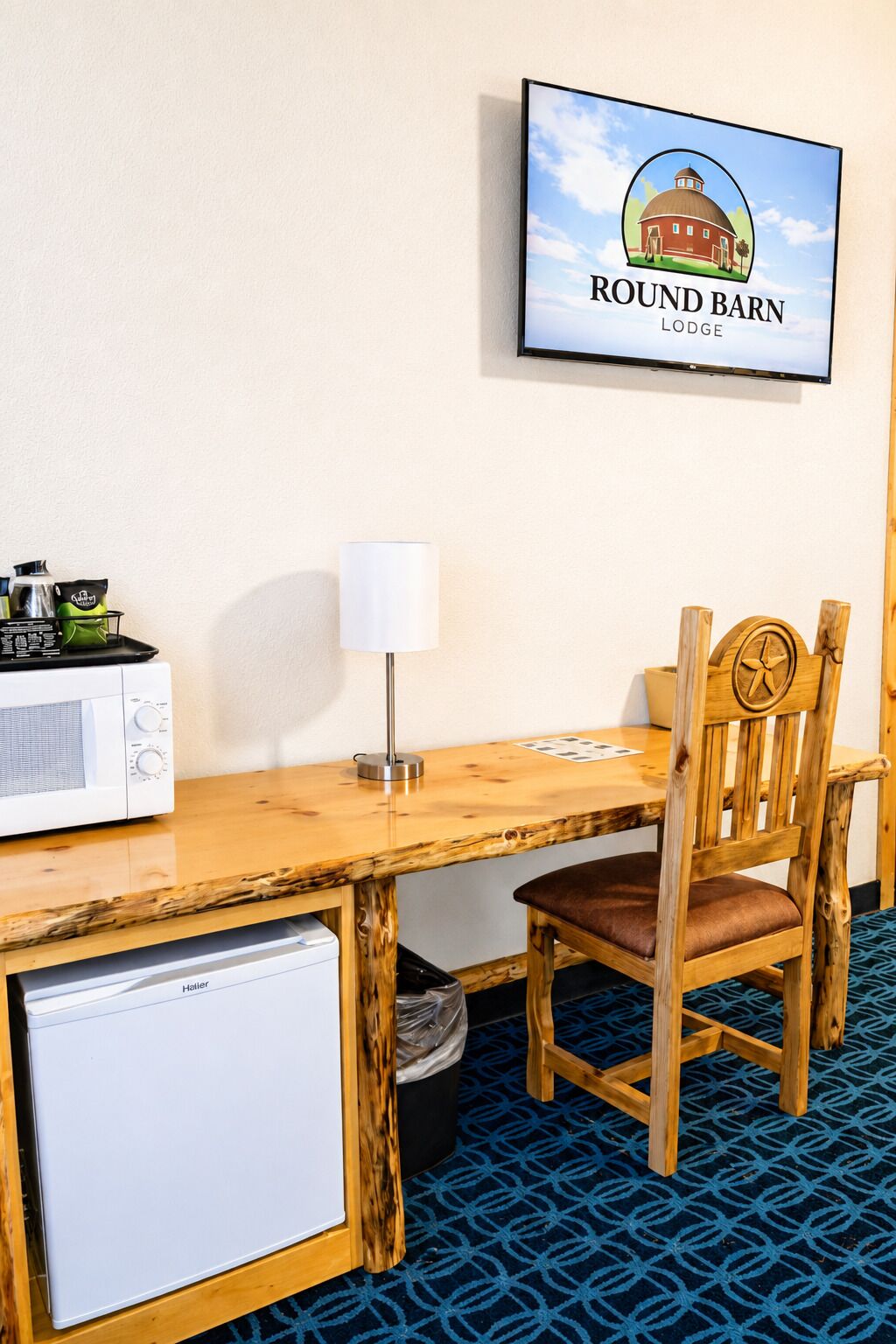 Habitación de hotel con escritorio de madera, una silla, televisor montado en la pared, refrigerador pequeño y un cesto de basura.