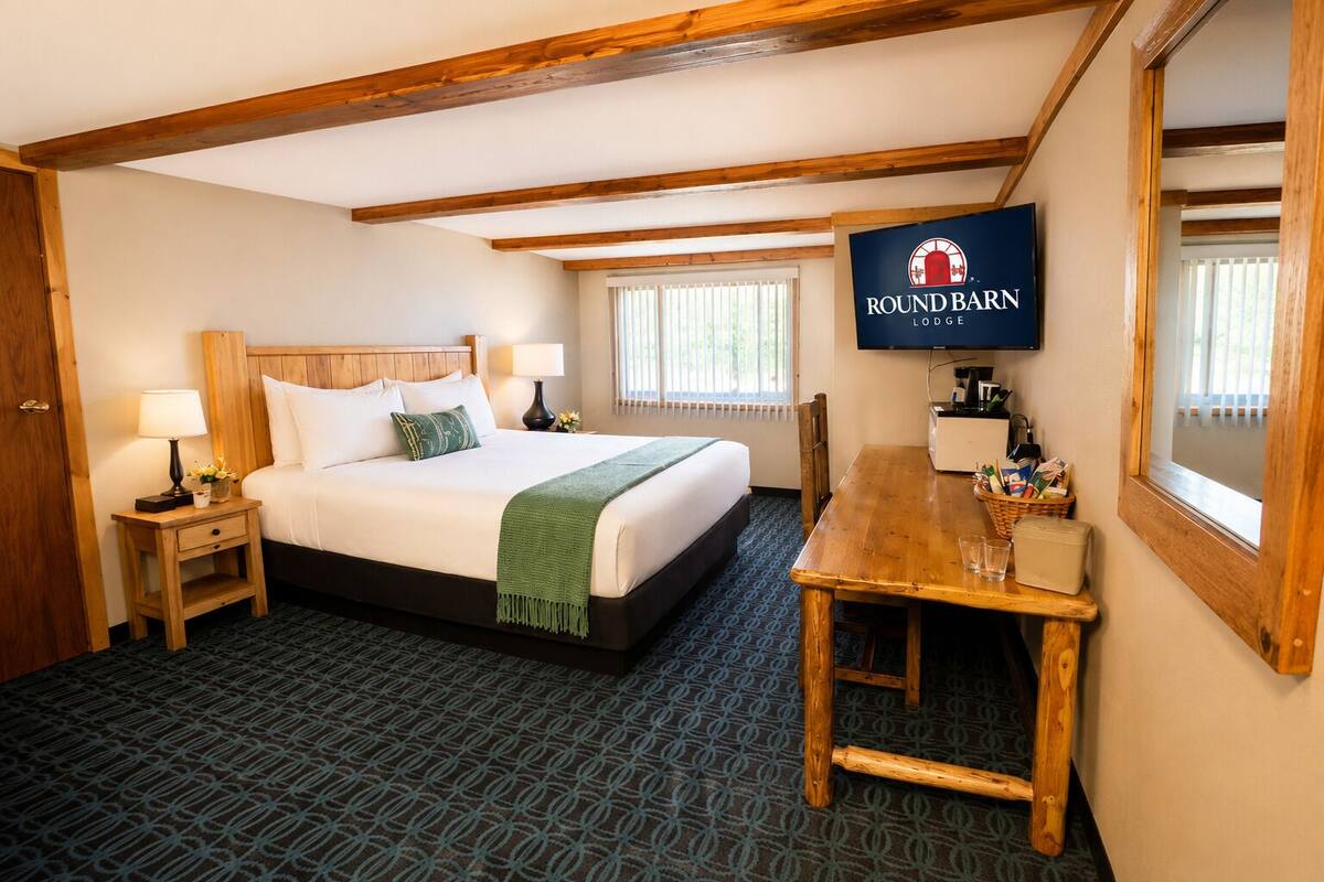 Une chambre d’hôtel comprenant un lit, des tables de chevet, un téléviseur, une table à manger en bois et une fenêtre.