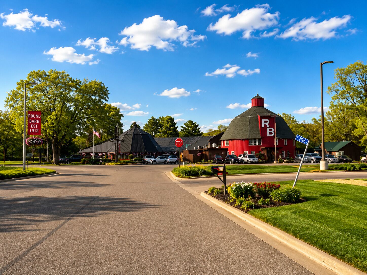 A red building with a distinctive roof, a stop sign, and a street sign indicating 'Round Barn Est 1912.'