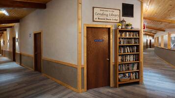 A hallway with a wooden door labeled 'Office Supply,' a bookshelf with books, and a sign reading 'Welcome to the Lending Library at Round Barn Lodge.'