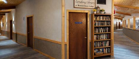 A hallway with a wooden door labeled 'Office Supply,' a bookshelf with books, and a sign reading 'Welcome to the Lending Library at Round Barn Lodge.'