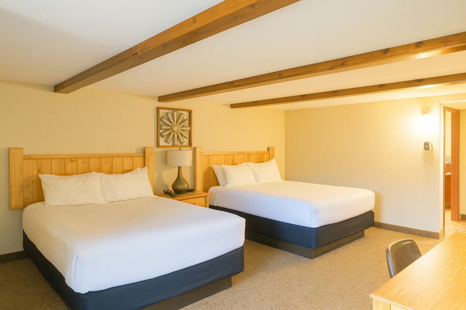 Una habitación de hotel con dos camas, techo de madera, una lámpara y un escritorio.