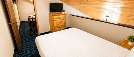 A bedroom with a bed, a dresser, a television, and a small plant.