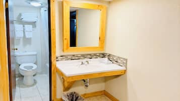 A bathroom with a white sink, wooden vanity, a mirror, and a toilet visible through an open door.