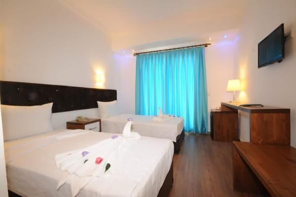 A hotel room with two beds, a desk, a chair, a TV, and a window with curtains.