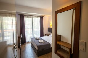 A hotel room with a bed, a desk, a chair, a large mirror, and a window with curtains.