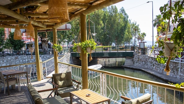 Un espacio al aire libre con mobiliario de mimbre, una pared de piedra y vistas a un canal con un puente.