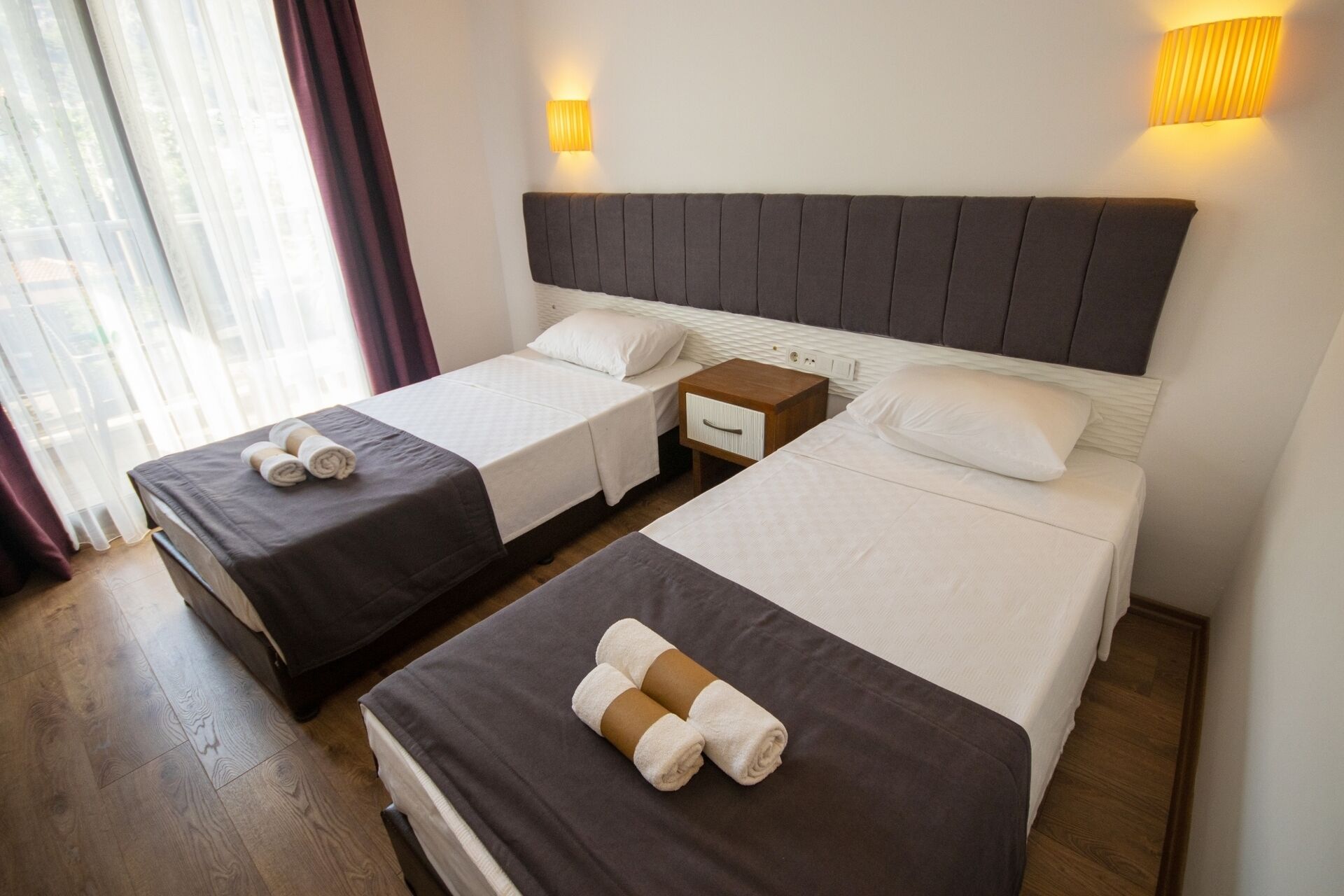 A hotel room with two beds, each with a wooden nightstand and a lamp.