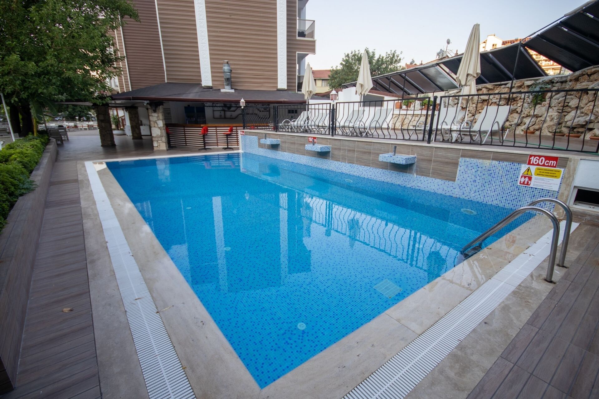 Una piscina rectangular con borde de azulejos, barandilla metálica y señal de seguridad que indica una profundidad de 160 centímetros.