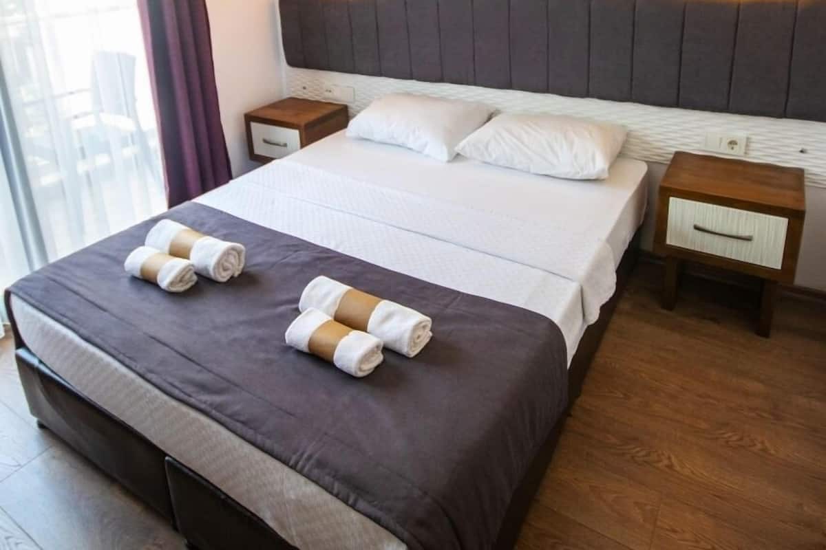 A hotel room with a large bed, two bedside tables, and a window with curtains.