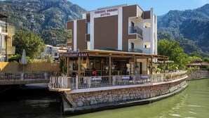 Un restaurante y bar a orillas del río, con pared de piedra y vistas a las montañas.