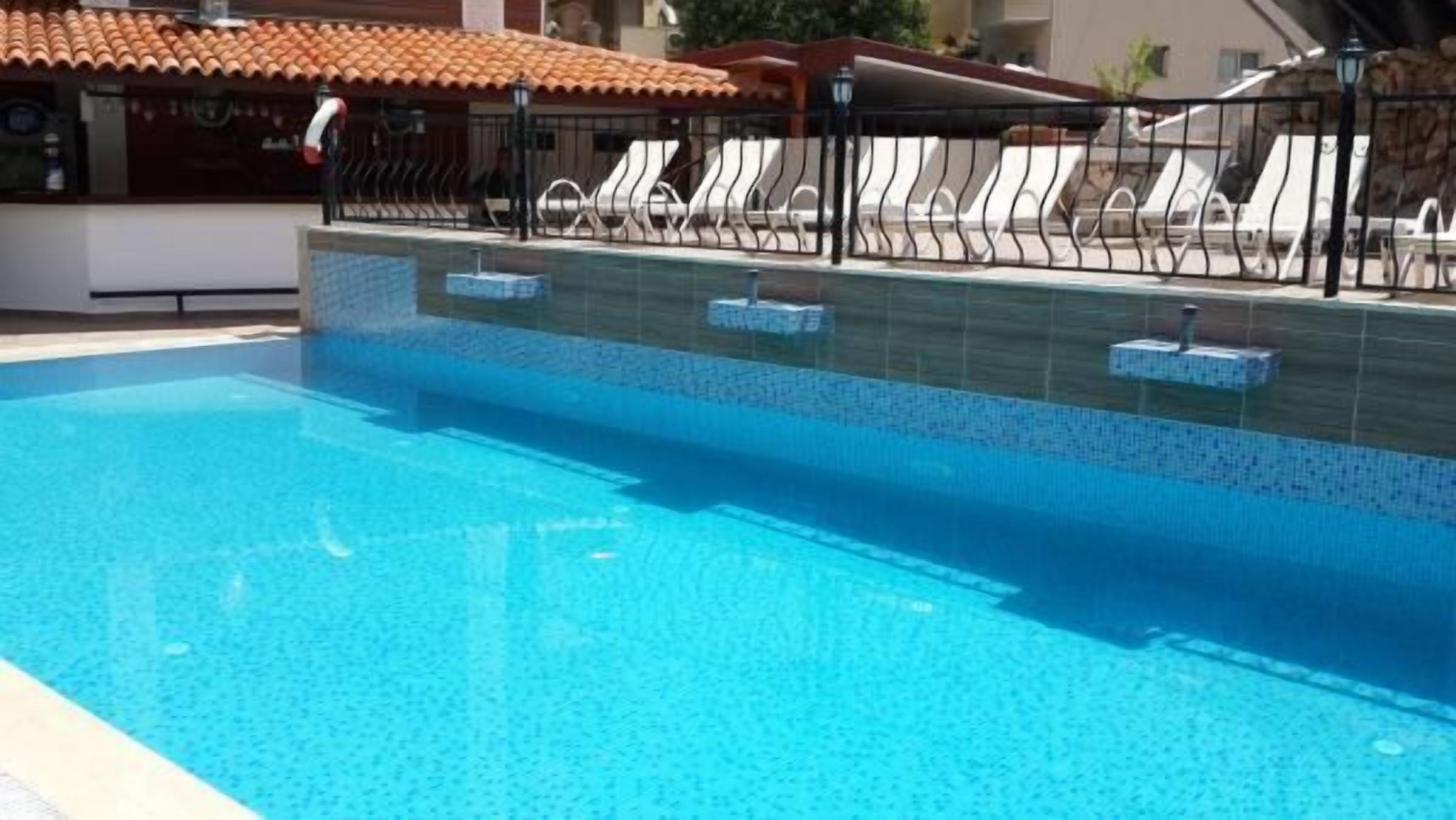 A swimming pool with clear blue water, surrounded by a tiled deck and a metal fence.