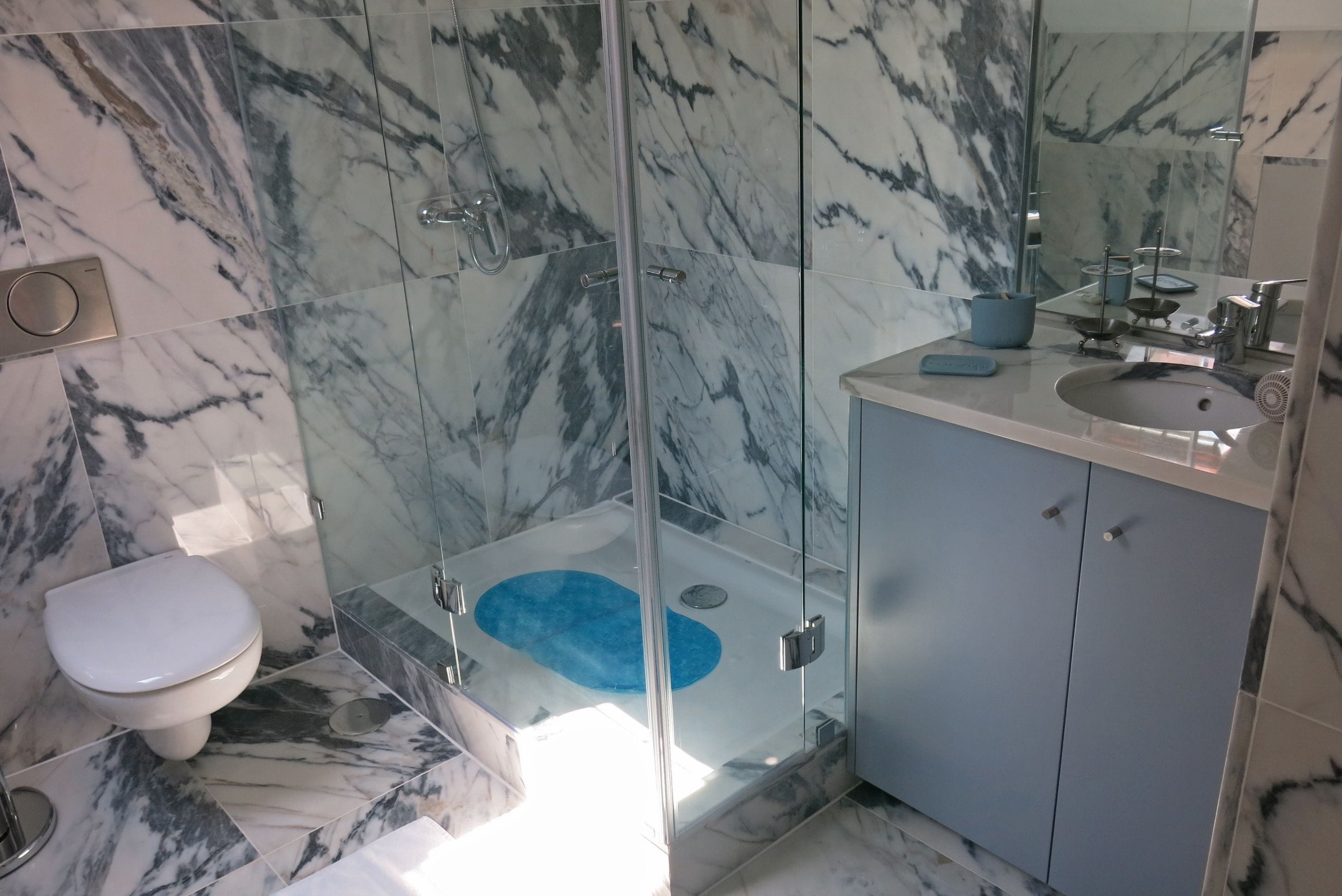 Une salle de bain avec une douche à parois de verre, des toilettes et un lavabo surmonté d’un tapis bleu.