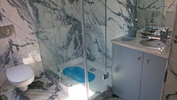 Une salle de bain avec une douche à parois de verre, des toilettes et un lavabo surmonté d’un tapis bleu.