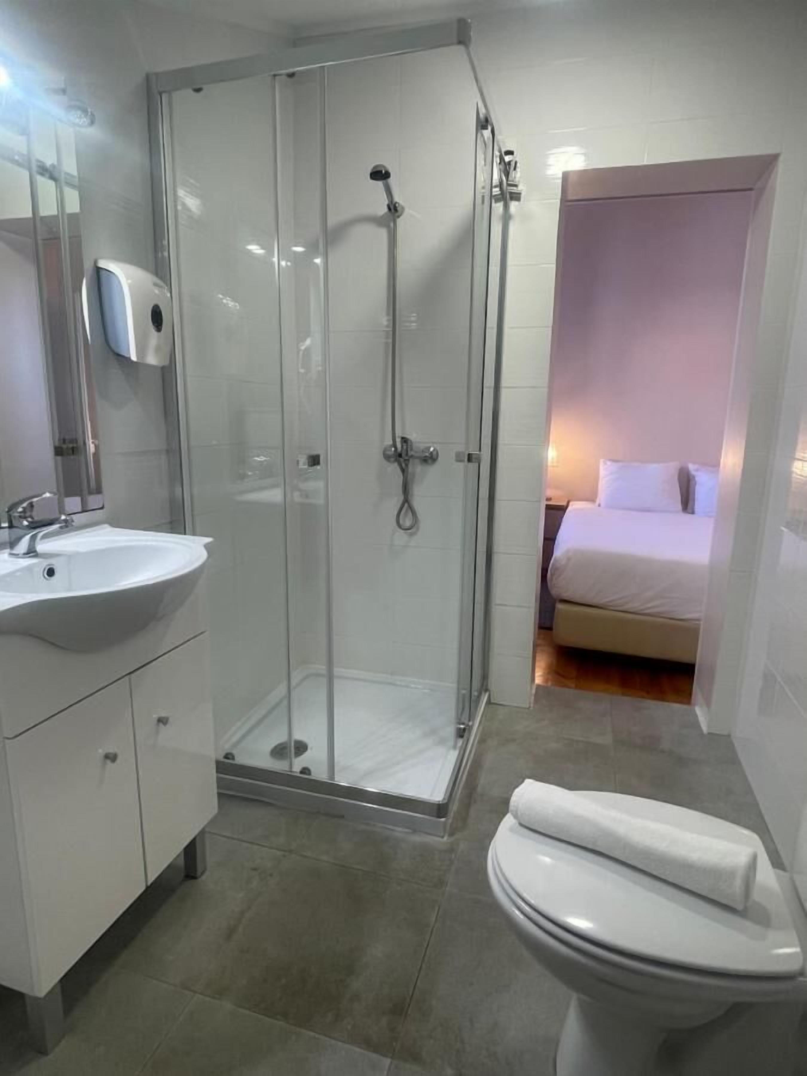 Een moderne badkamer met een douche met glazen wand, een witte wastafel en een toilet.