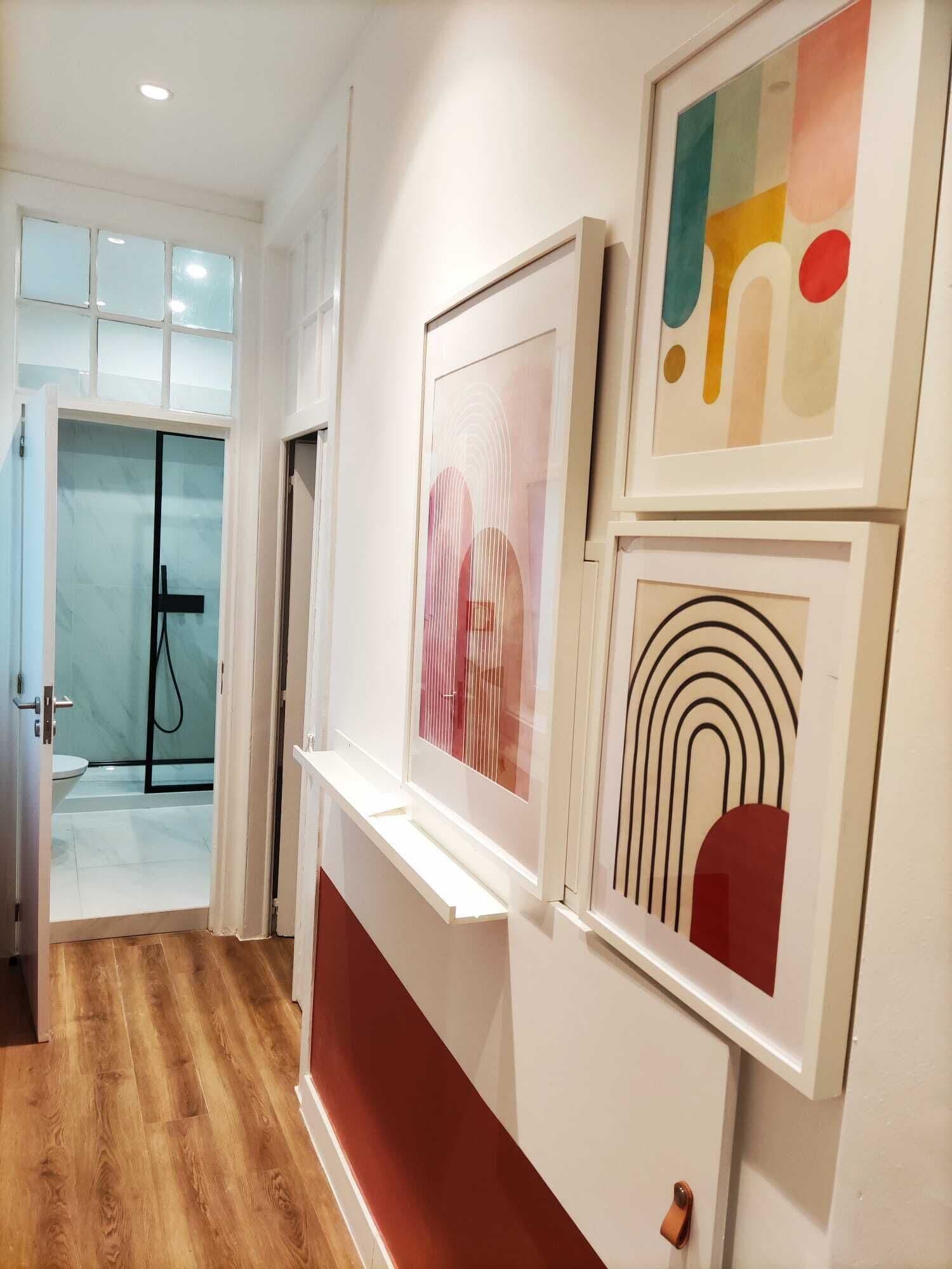 A hallway with a wooden floor, a glass shower enclosure, and three framed artworks on the wall.