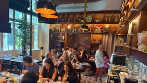 En restaurang med olika typer av sittplatser, inklusive bord och avskilda bås. Det finns flera hyllor med flaskor och dekorativa föremål. Golvet har ett geometriskt mönster av kakelplattor.