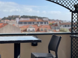 A balcony with a table and chairs, overlooking a cityscape with red-roofed buildings. - Lisbon Colours Bairro Alto Apartments (Lisbon)