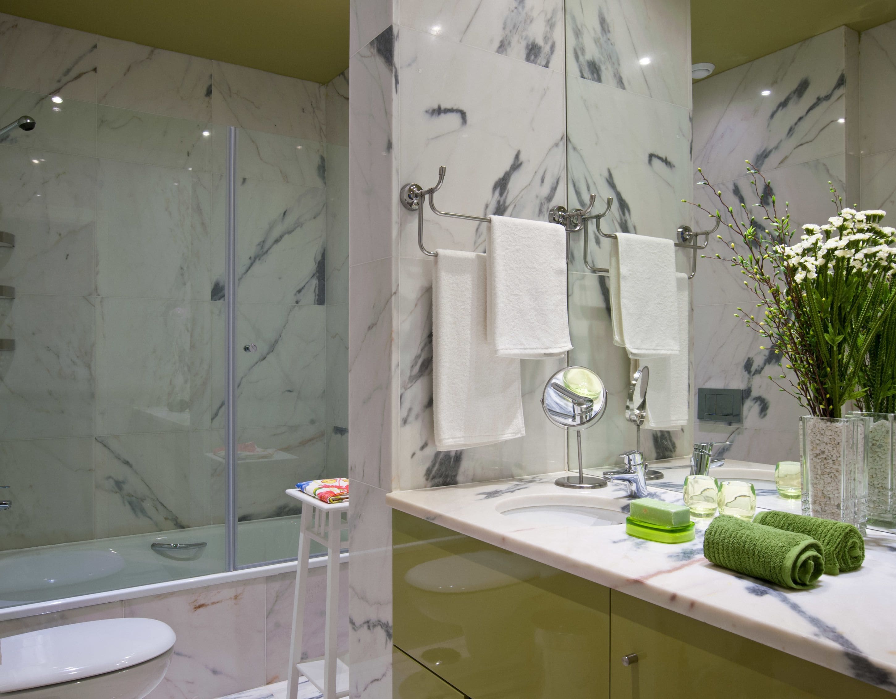 Ein Badezimmer mit einer Marmordusche, einer Toilette, einem Waschbecken mit Spiegel und einer Vase mit Blumen.