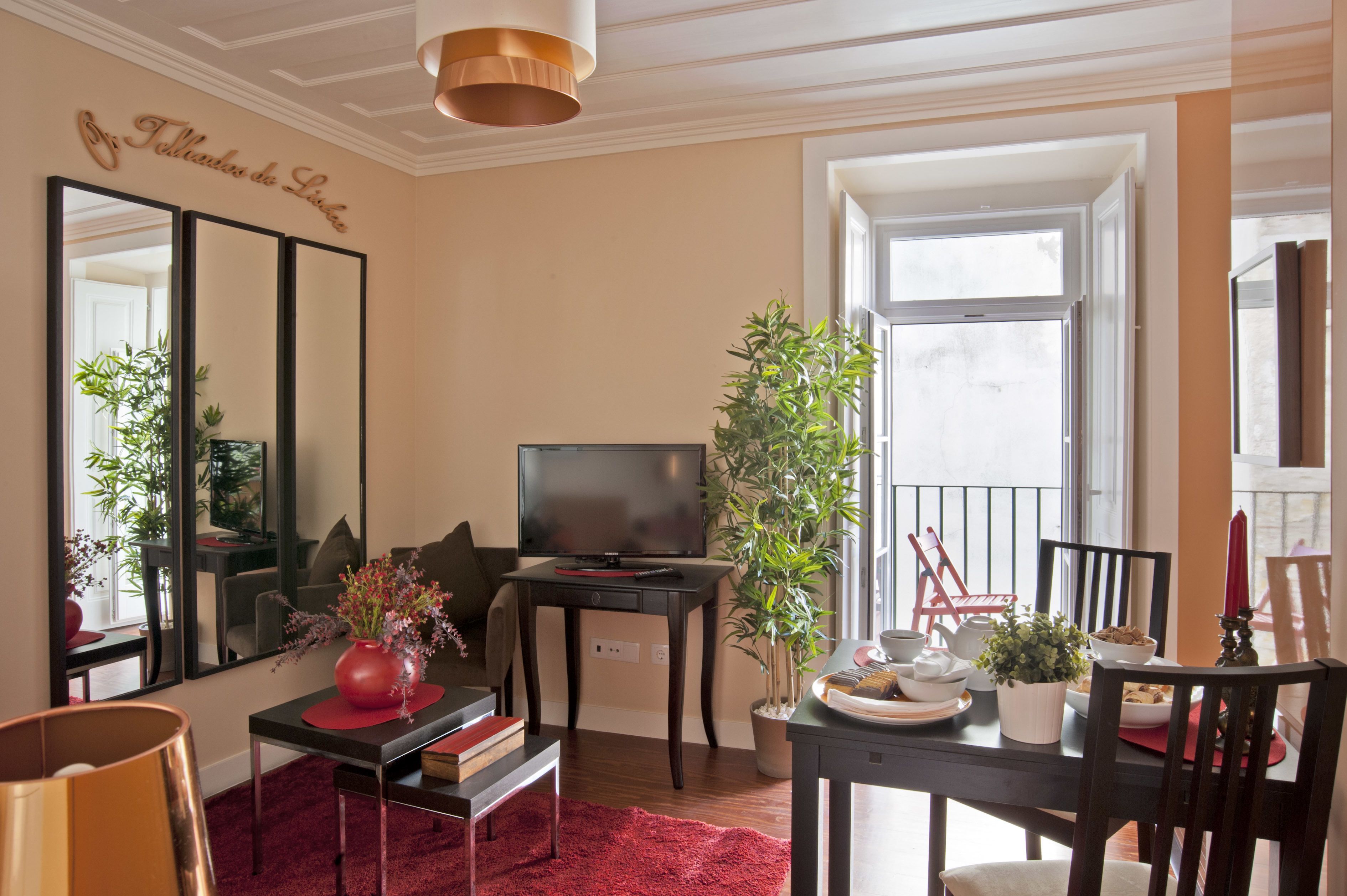 Una sala de estar con televisión, una mesa de comedor con sillas, un tapete rojo y un espejo grande.
