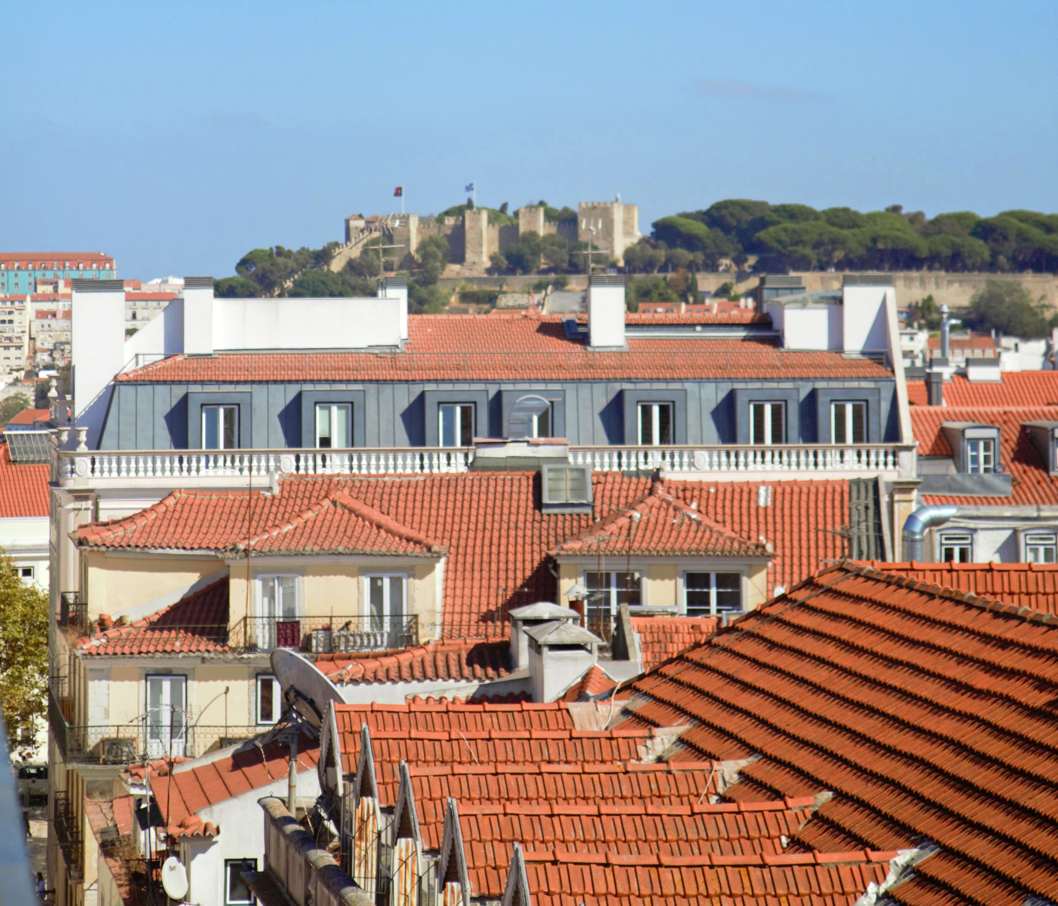 Filetta di edifici con tetti in tegole rosse e un castello sullo sfondo.