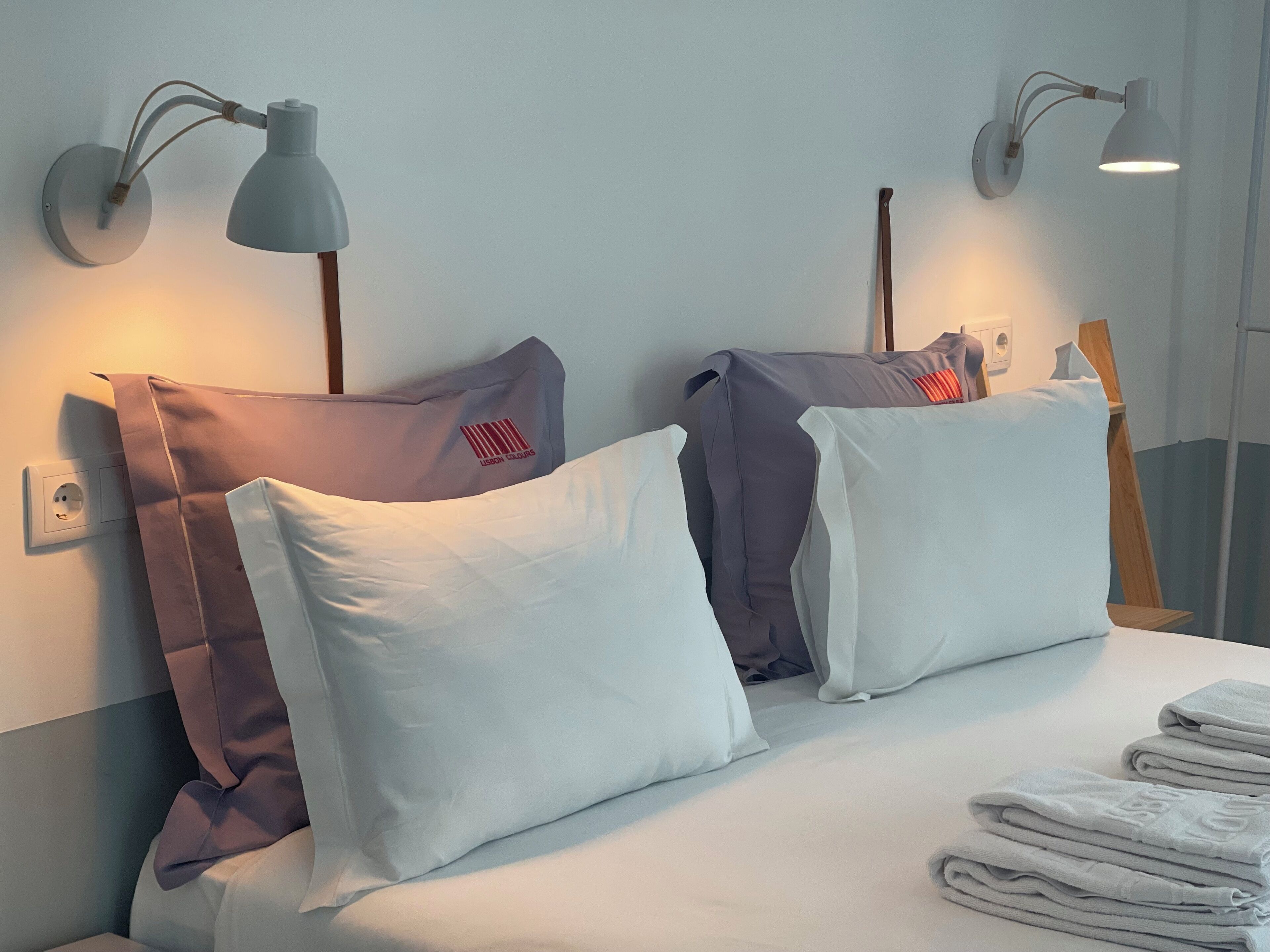 Een hotelkamer met twee bedden, elk voorzien van witte en bruine kussens, en twee wandlampen.
