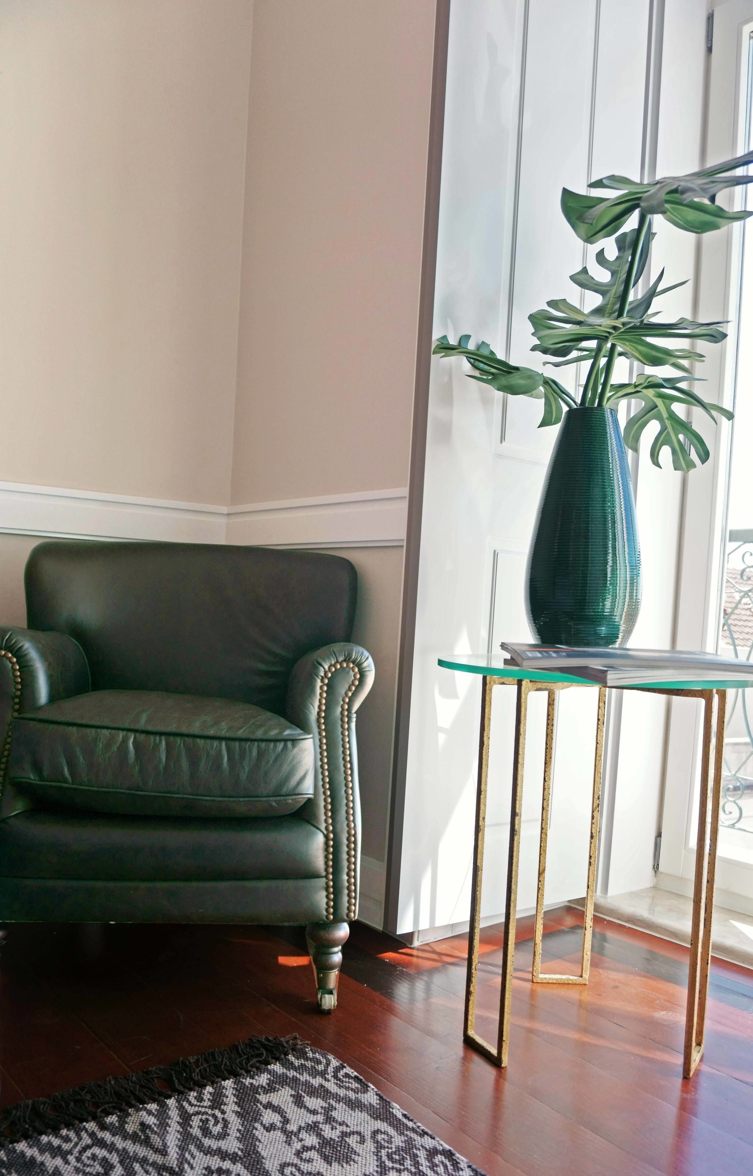 A room with a dark green leather armchair, a glass-top side table with a green vase, and a patterned rug.