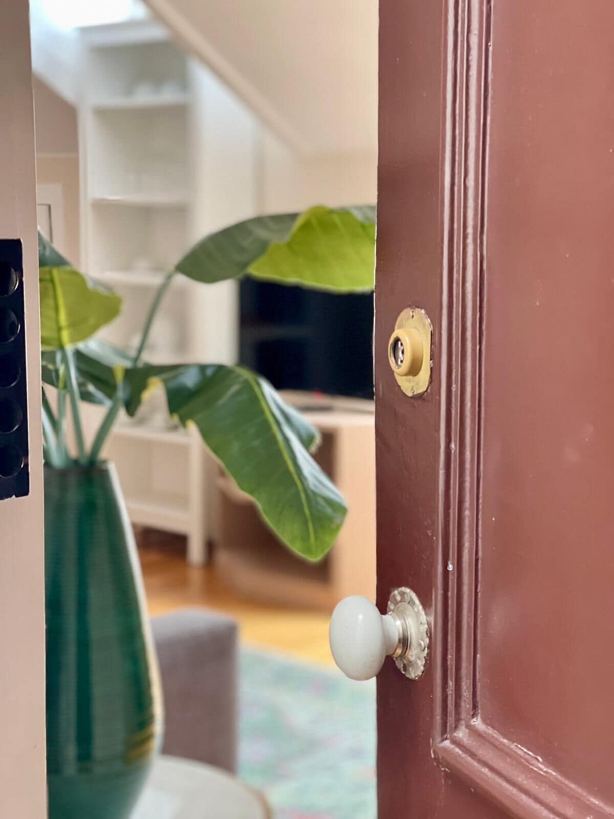 Uma porta marrom com uma maçaneta redonda, uma fechadura e uma pequena placa de latão.