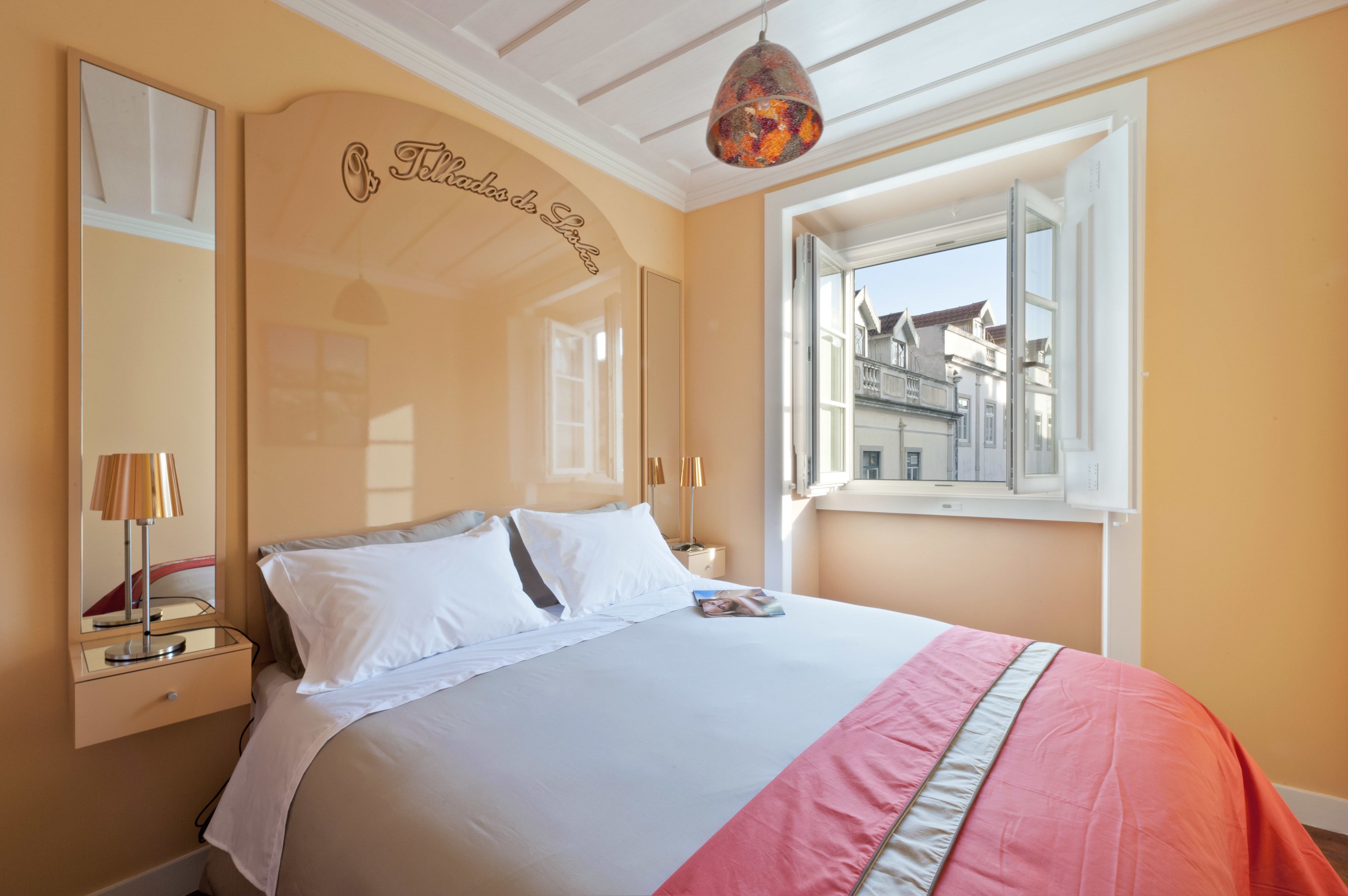Ett hotellrum med en säng, ett nattduksbord, en lampa, ett fönster och utsikt över byggnaderna utanför.