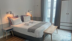 Ett modernt sovrum med en säng, sängbord, en bänk, en garderob och utsikt över omgivningen.