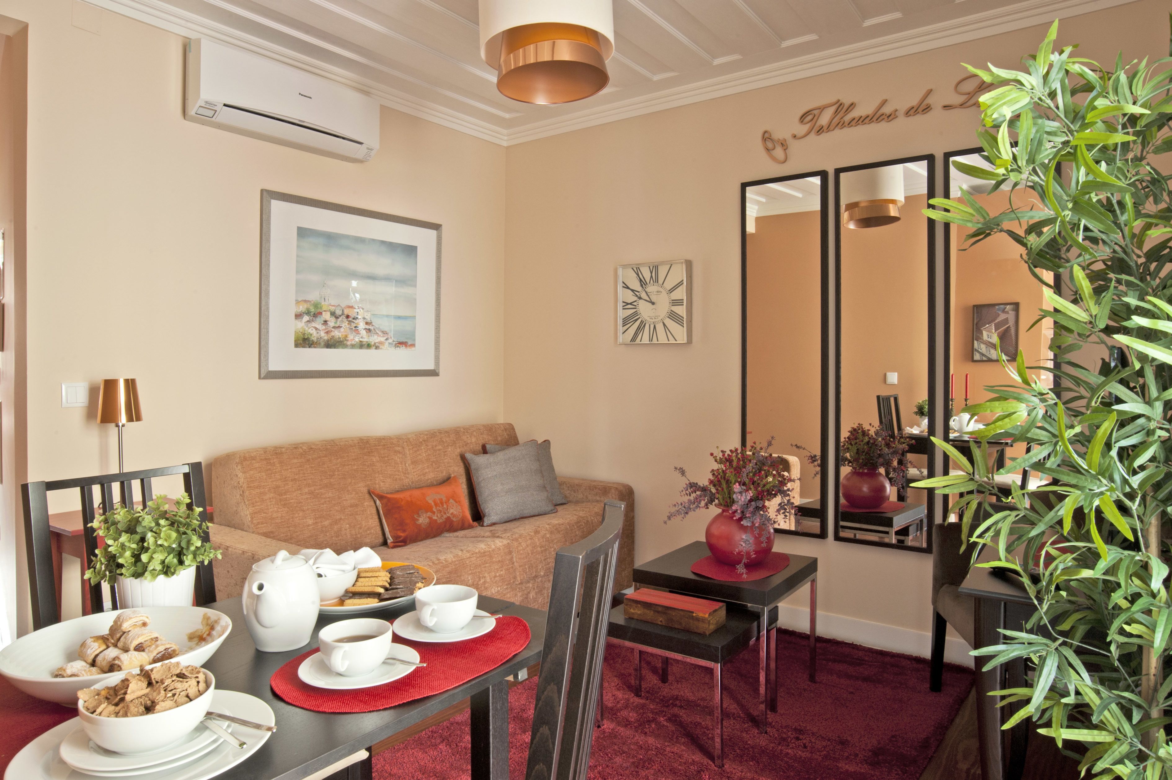 A cozy room with a sofa, a dining table with a red placemat, a vase with flowers, and a mirror reflecting the room.