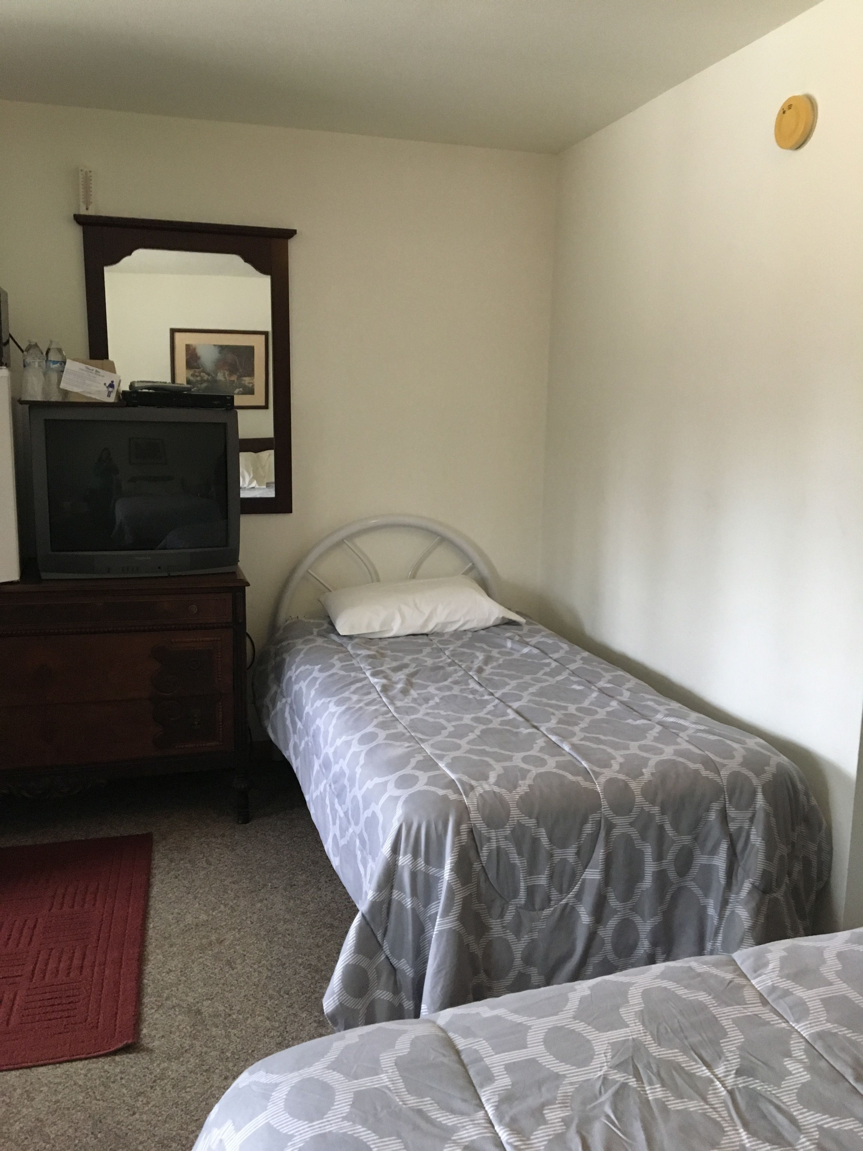 A bedroom with two single beds, a wooden dresser, a television on top, and a mirror on the wall.