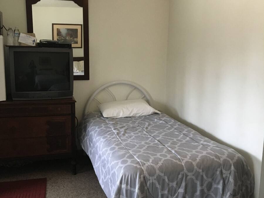 Ein Schlafzimmer mit zwei Einzelbetten, einer Holzkommode, einem Fernseher darauf und einem Spiegel an der Wand.