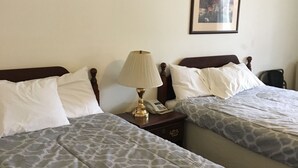 Hotelkamer met twee bedden, elk met een beddekleed met dessin, een nachtkastje met een lamp en een ingelijste foto aan de muur.
