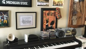 Een kamer met een piano, ingelijste posters aan de muur en een stapel CD's.