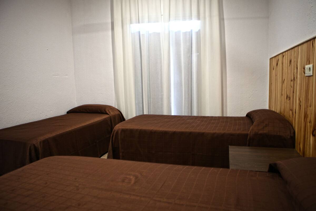 A room with three single beds, a wooden wall panel, and a window with curtains.
