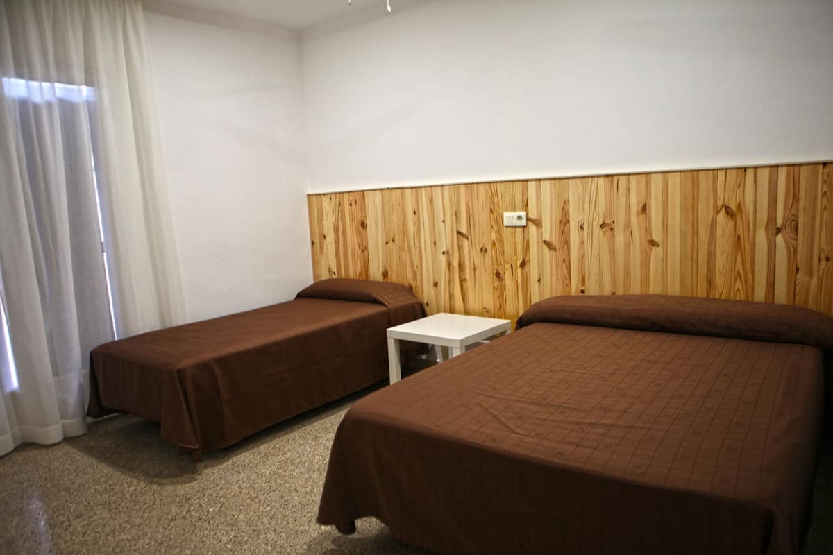 A hotel room with two single beds, a small white table, and a wooden headboard.