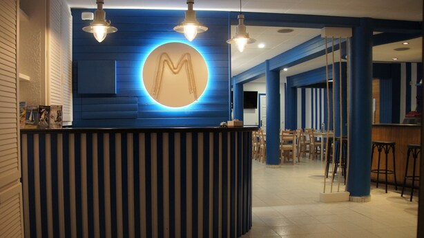 A reception area with a blue and white striped counter, overhead lighting, and a circular wall decoration. - Hostal Miranda (Blanes)